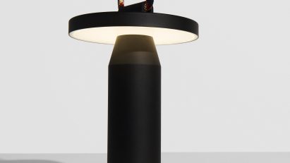 Black lamp with rainbow coloured cord on white table in front of white wall