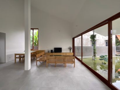 Interior of a concrete room with wooden furniture and wood-framed sliding doors overlooking a pond