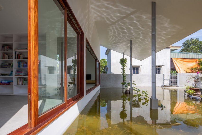 A pond surrounding a home with white walls and wood-framed windows