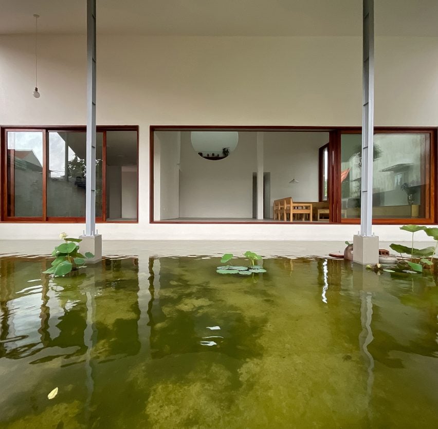 A pond surrounding a home with white walls and wood-framed windows