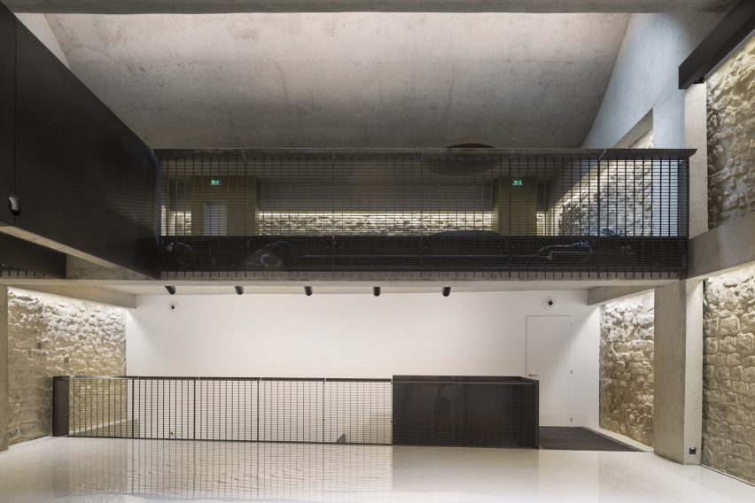 A room with glossy white floors, mezzanine level with black railings and white brick walls