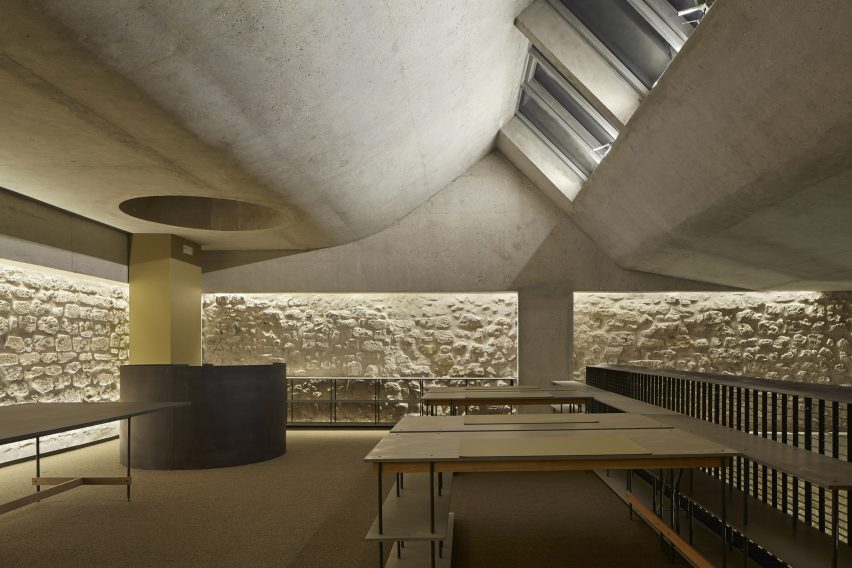 A room with a curved concrete ceiling, skylights and white brick walls