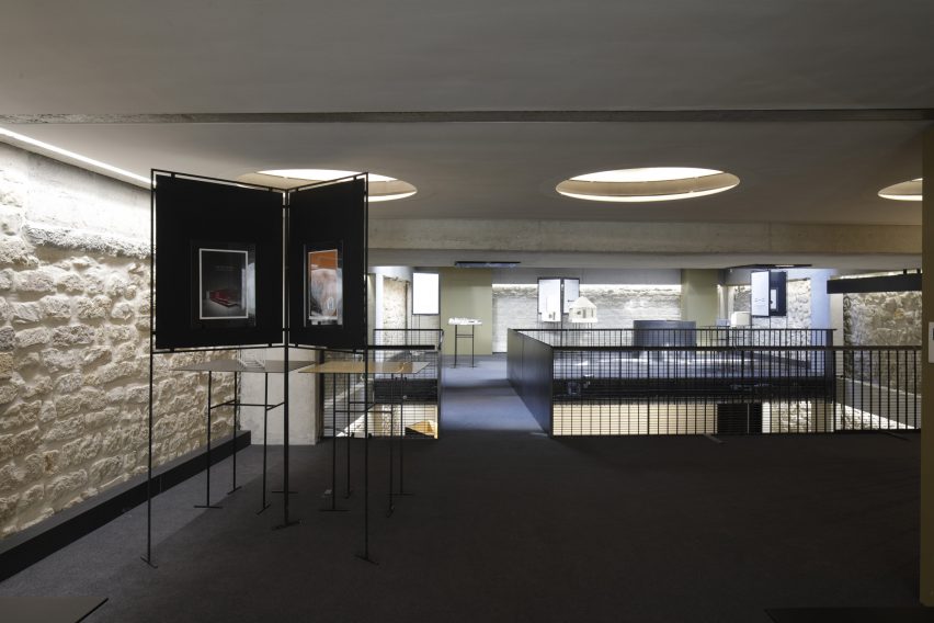 A room with dark carpets, white brick walls, circular recessed ceiling lights and freestanding displays
