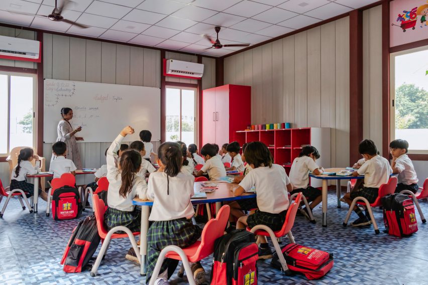 Students in a classroom interior with red chairs and white walls