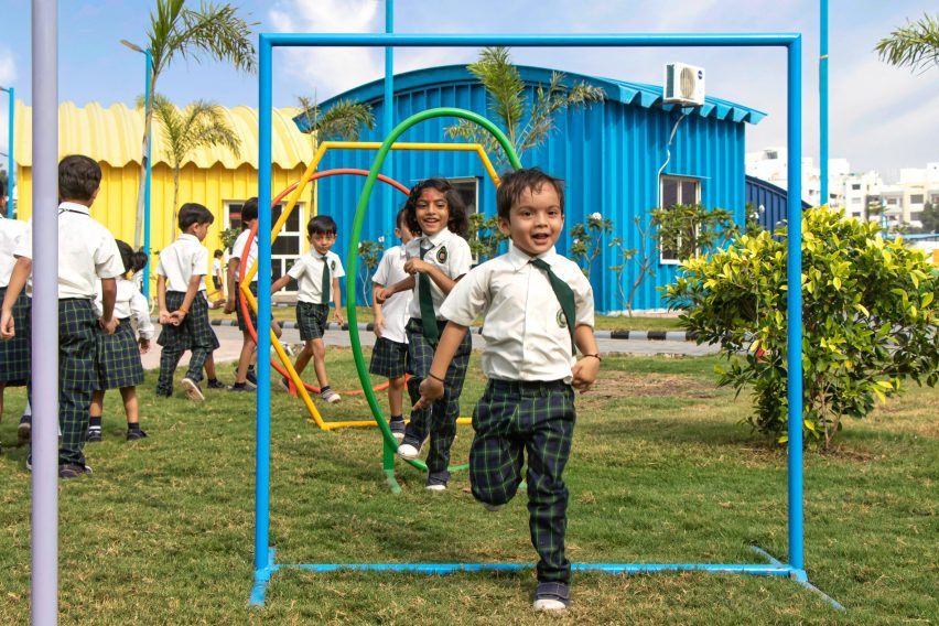 Children playing on a playground with a blue metal school building behind