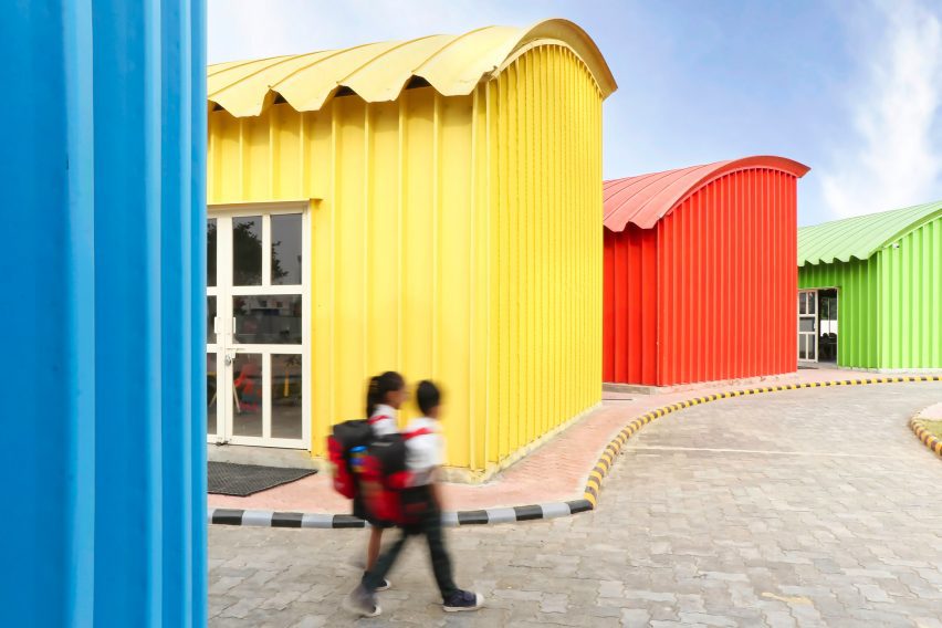 School children walking beside blue, yellow, red and green steel buildings