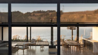 Exterior of a one-storey open-plan home with glazed walls overlooking the sea
