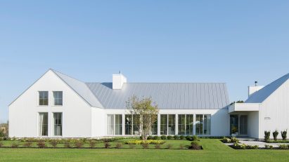 A white U-shaped house with a pitched roof on a green lawn