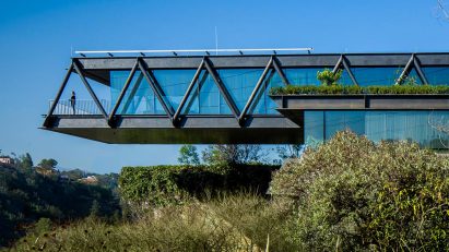 One-storey house with a ddark metal structure cantilevering over bushes