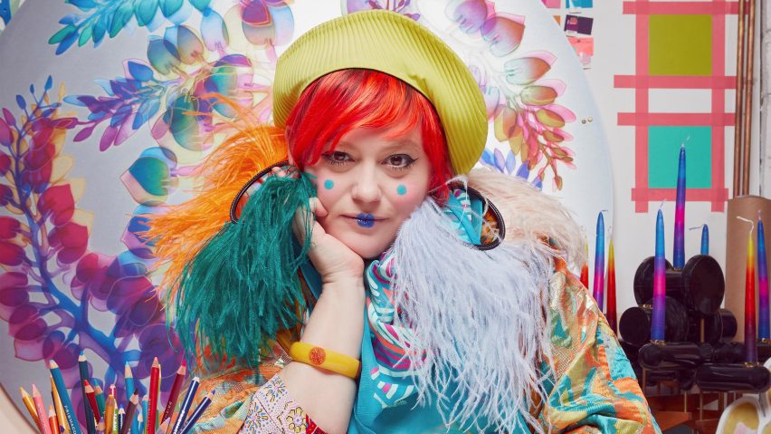 Person with red hair and green beret sitting at a table with colouring pencils