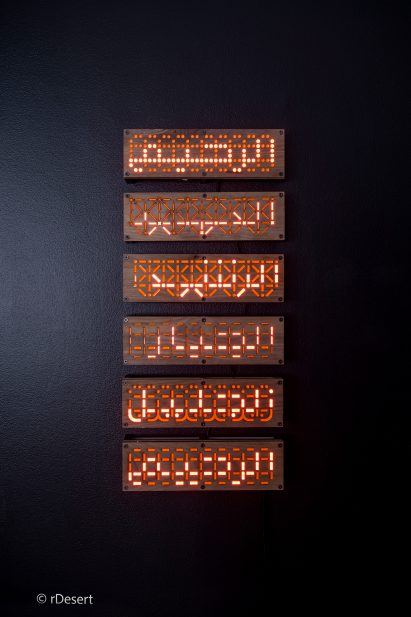 Six wooden panels mounted on dark wall with lit up Arabic text on each