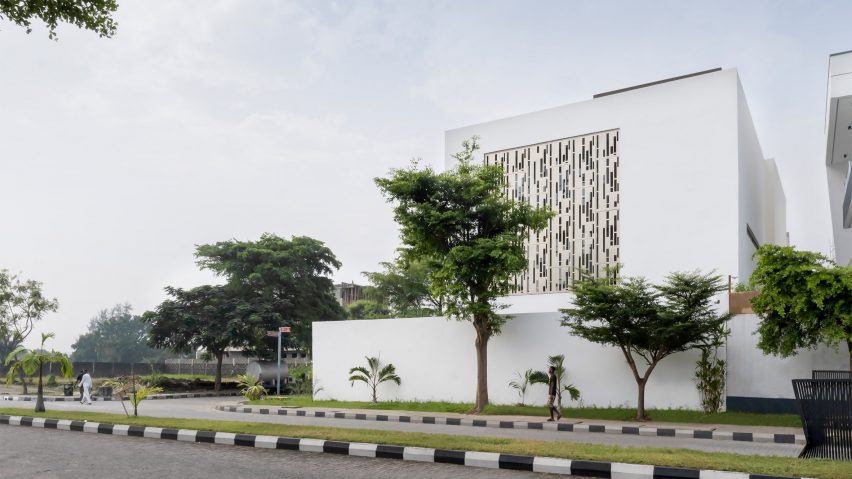 White cube house with a perforated metal opening in the facade on a street corner