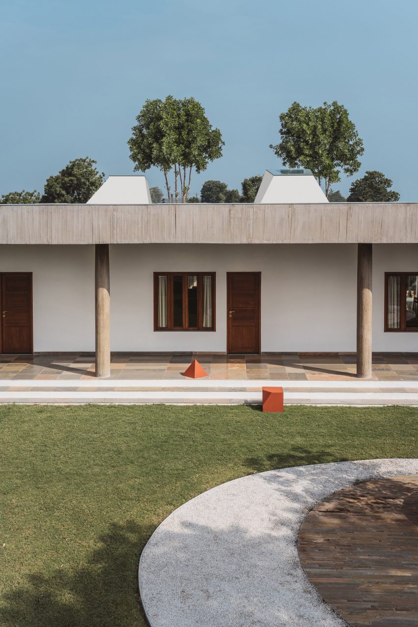 Grass garden in front of a one-storey home with white walls and concrete structure