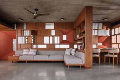 A living room with polished concrete floors, wood-panelled walls and a grey L-shaped sofa