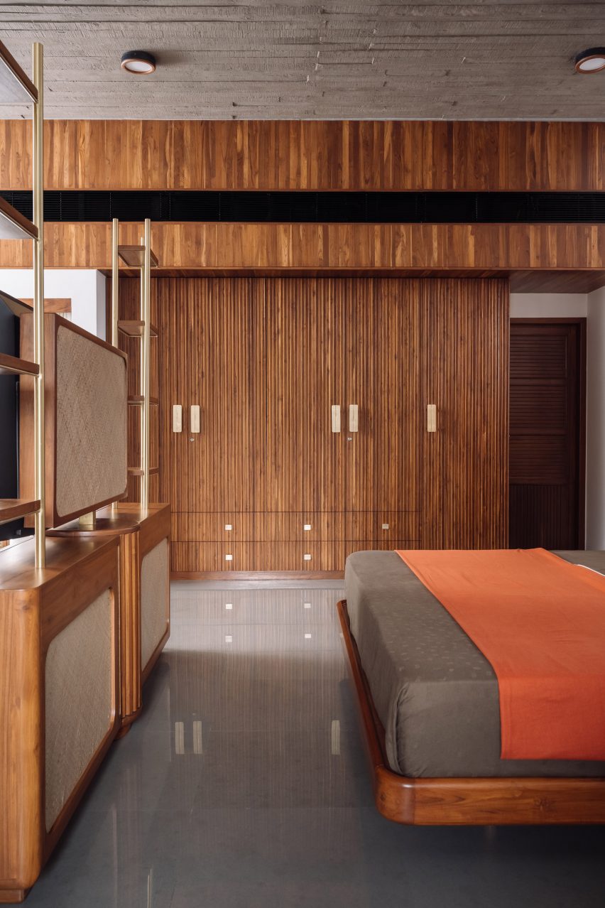 A bedroom with wood-panelled walls, concrete floors and a red throw over the bed