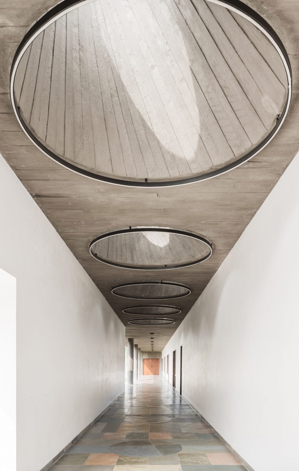 Coridoor with white walls and concrete ceiling with circular skylights
