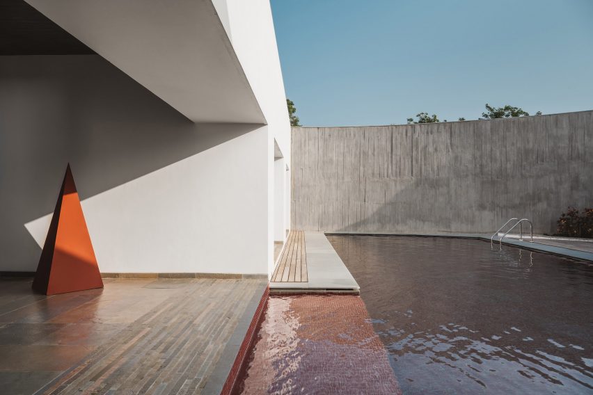 Outdoor swimming pool with red tiles next to a white house