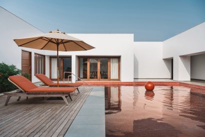 Swimming pool with red pool tiles and timber decking in front of a white house