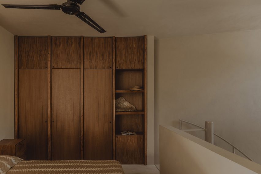 A bedroom with wood wardrobes on a mezzanine level in a concrete home by FMT Estudio