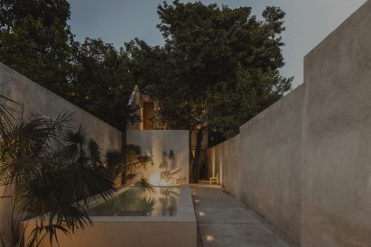 Concrete courtyard with a small swimming pool, concrete perimeter walls and lush green trees