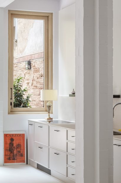 Kitchen of House 1616 with white cabinets, white floors, white walls and a wood-framed window