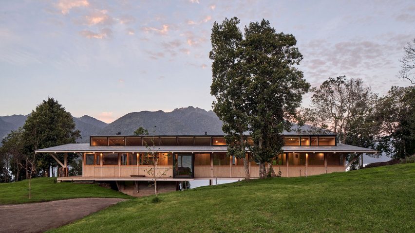 Timber house extending across a hillside overlooking a lake