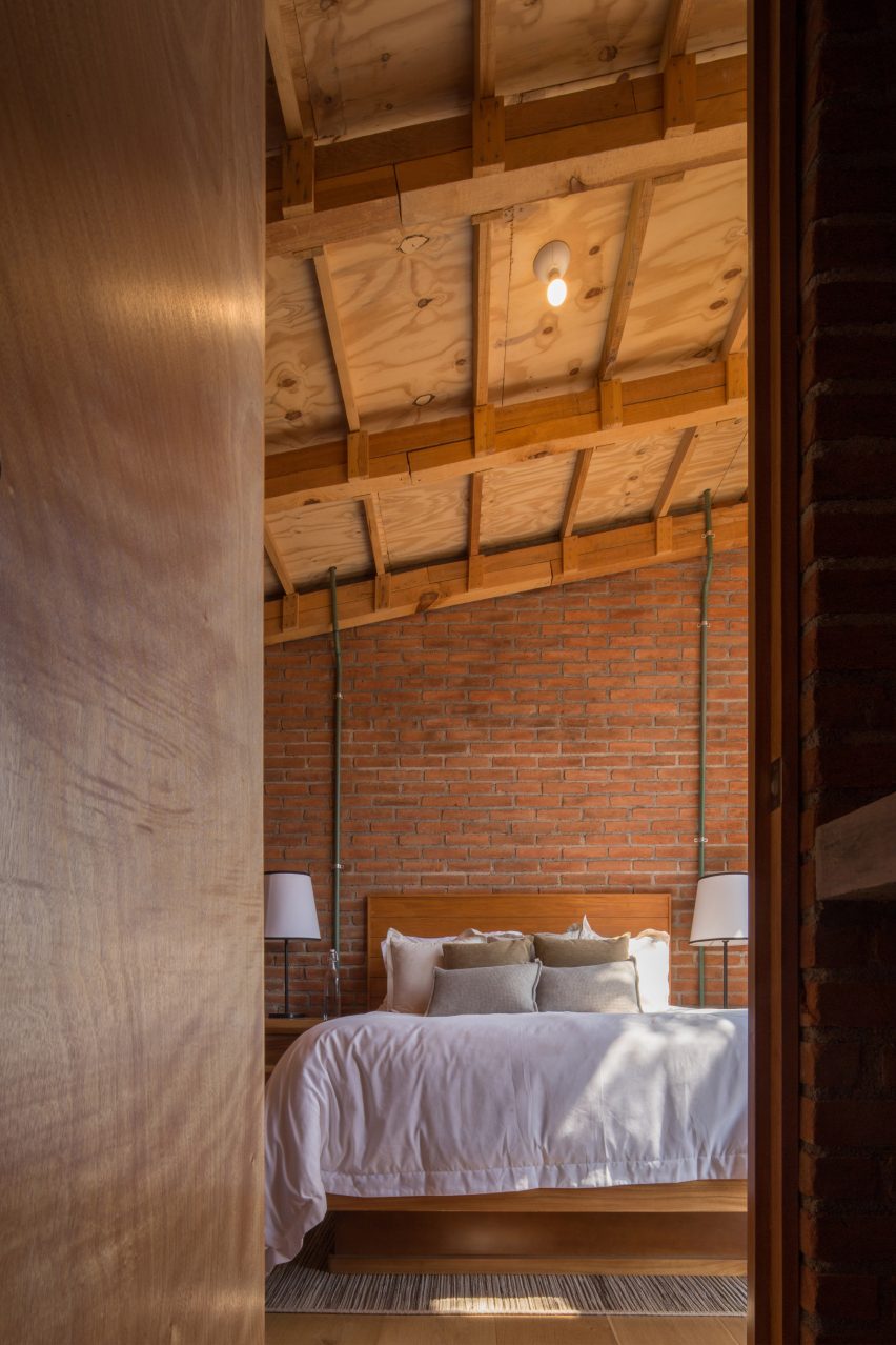 Bedroom with brick walls, wooden ceiling structure and a bed with white bedding