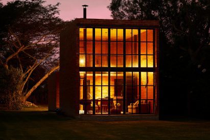 Exterior of a brick micro home with double-height window facade lit up at night