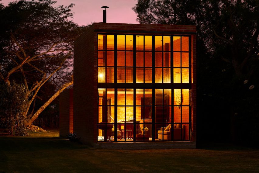 Exterior of a brick micro home with double-height window facade lit up at night