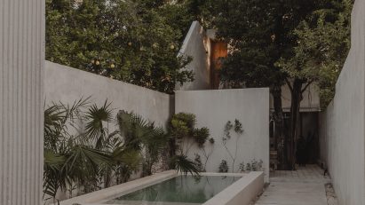 Concrete courtyard with a small swimming pool, concrete perimeter walls and lush green trees