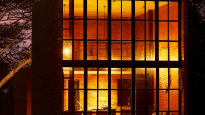Exterior of a brick micro home with double-height window facade lit up at night