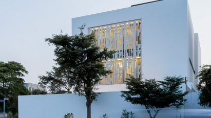 White cube house with a perforated metal opening in the facade on a street corner