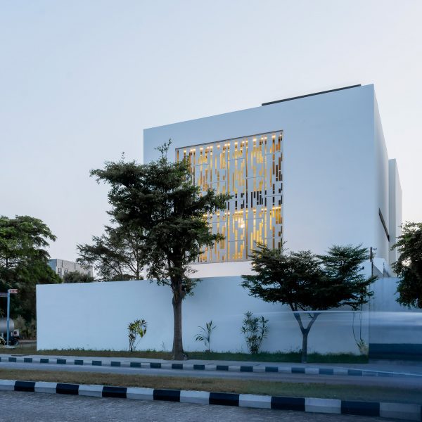 White cube house with a perforated metal opening in the facade on a street corner