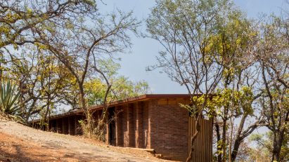 Wooden one-storey shed-like home on a sandy hill in Mexico with trees