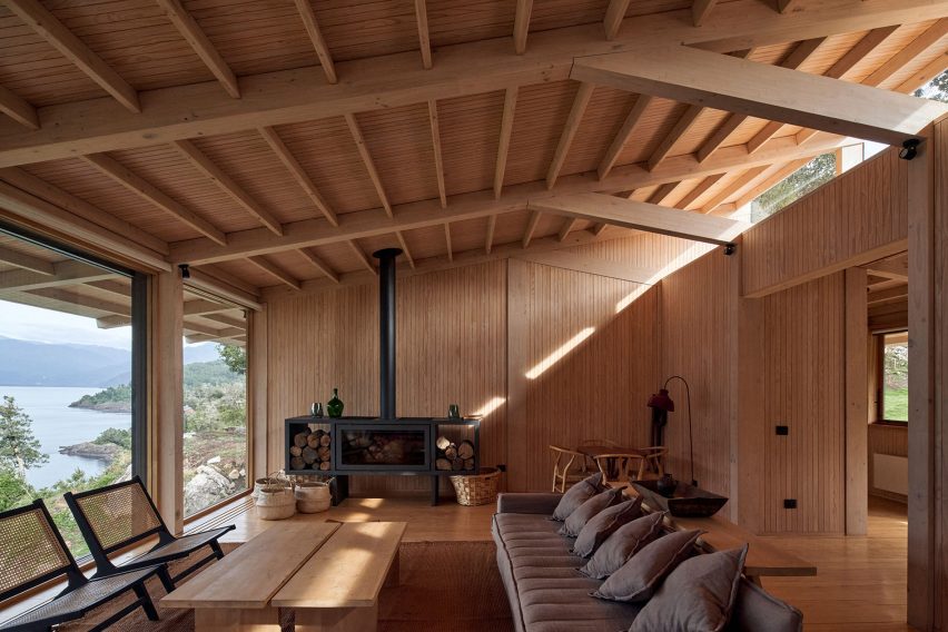 A living room in a timber structure with a pitched roof, decorated with a grey sofa, lounge chairs and a black fireplace