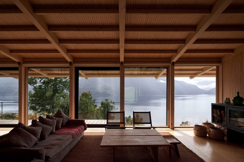 A living room with a grey sofa, lounge chairs and glass doors overlooking a lake