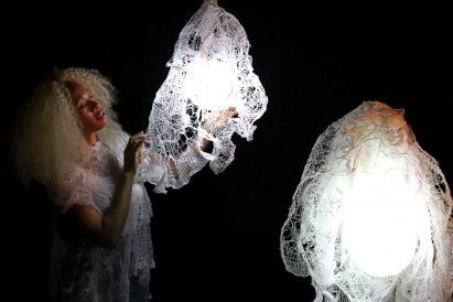 Student posing with lamps in front of black backdrop