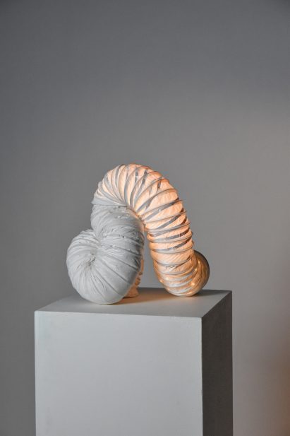 Tubular lamp on pedestal in front of grey backdrop