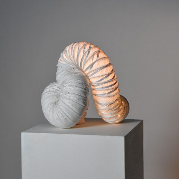 Tubular lamp on pedestal in front of grey backdrop