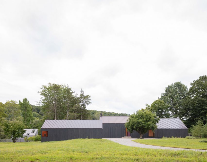 Three black timber barn-like buildings surrounded by trees