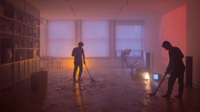 Silhouetted figures sweep the ground of the dark room 