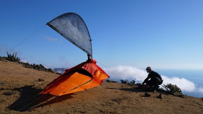 Photo of Pavel Hedström setting up his Fog-X jacket as a fog-catching mesh aerial in a bright outdoor setting with some low cloud cover in the background