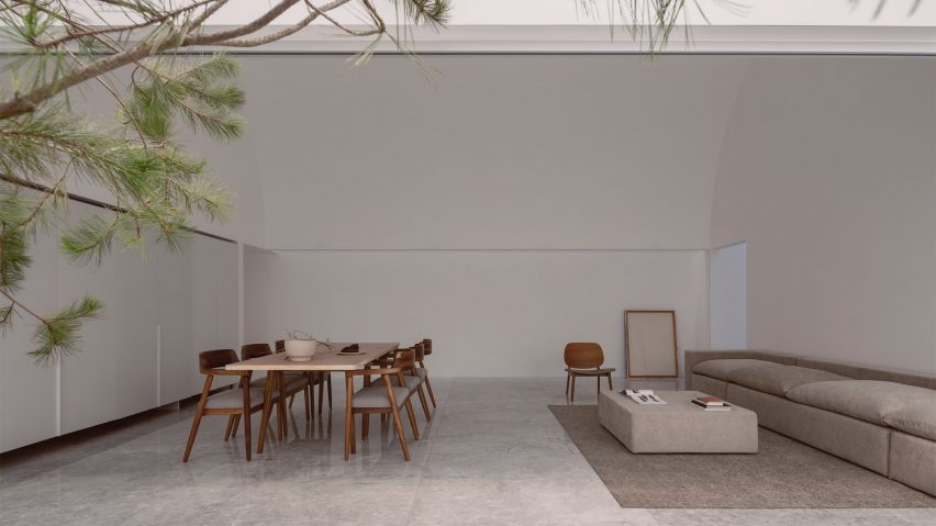 An open-plan living and dining room with white walls and floor, wooden dining table and chairs, and a grey sofa on a grey rug