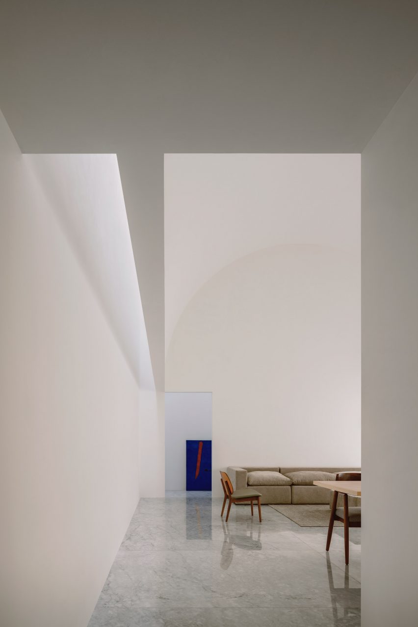 A white corridor leading to a living room with an arched ceiling and grey sofa