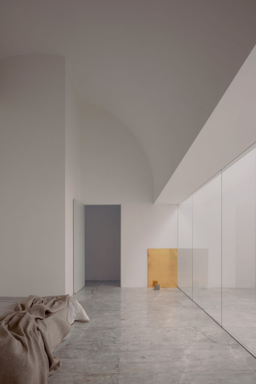 A bedroom with white walls, a curving ceiling and glass sliding door leading to a courtyard