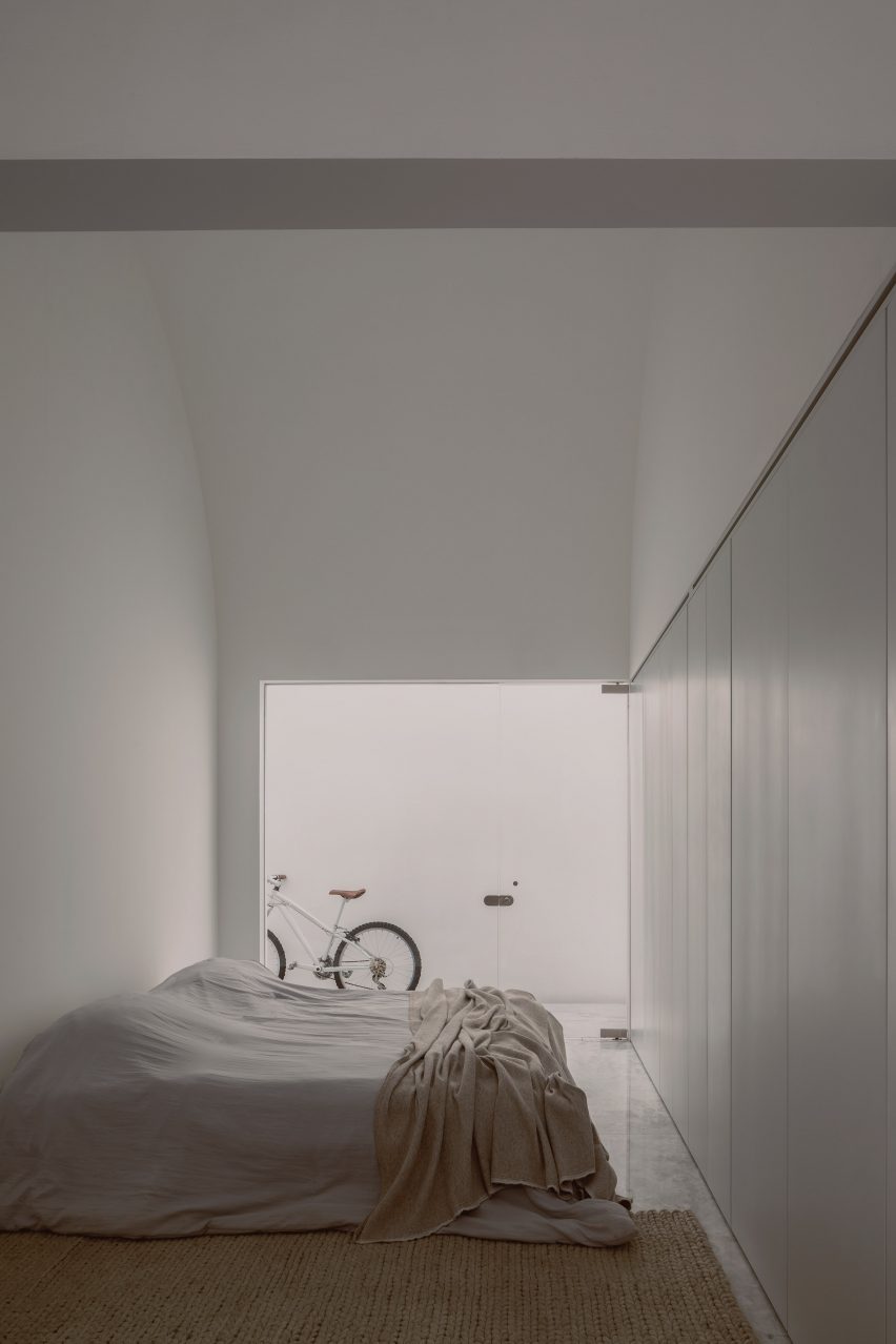 A white bedroom with a double bed and glass doors leading to an outdoor space with a bike