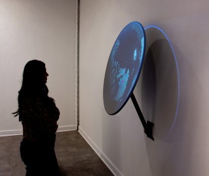 Figure looking at satellite dish mounted to wall in gallery space