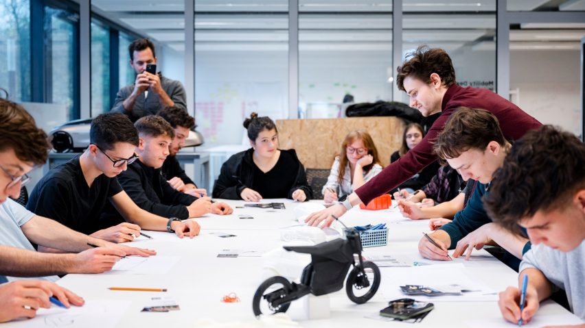 A photograph of a group of people sat around a white table, interacting with one another.