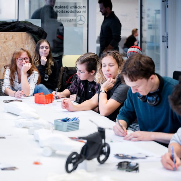 A photograph of a group of people sat at a white table, interacting with one another.