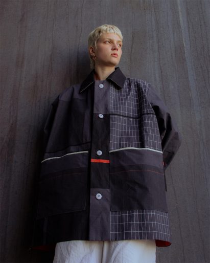 Model wearing dark overcoat in front of dark grey wall